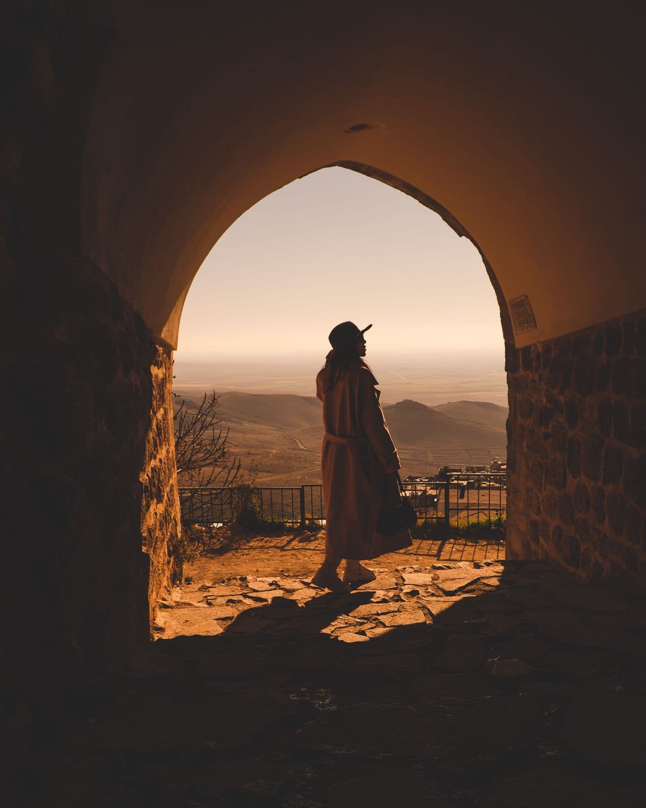 Silhouette of a traveler standing inside an ancient stone archway gazing over a desert valley