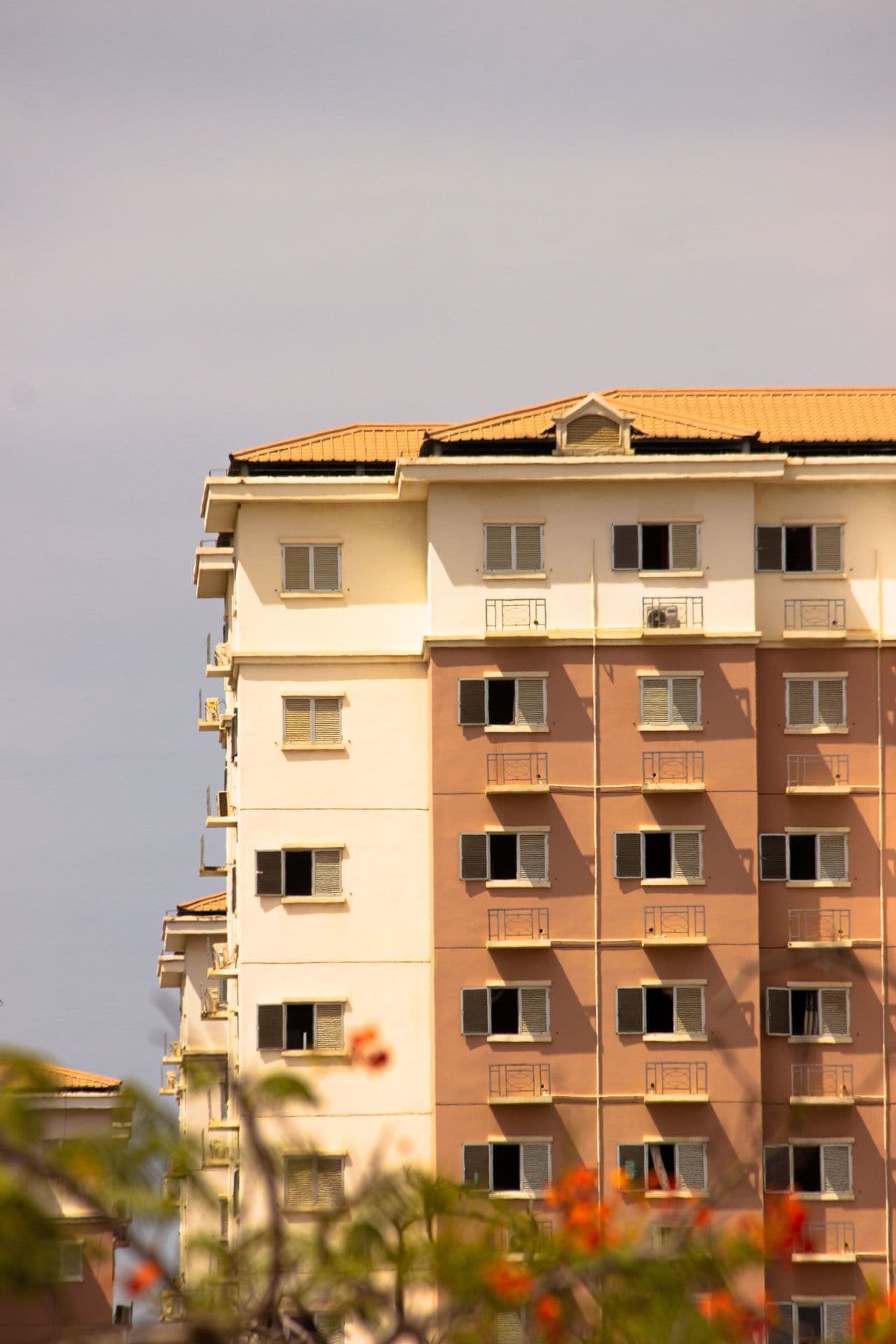 Multi-story terracotta and cream residential building with balconies framed by blooming red trees