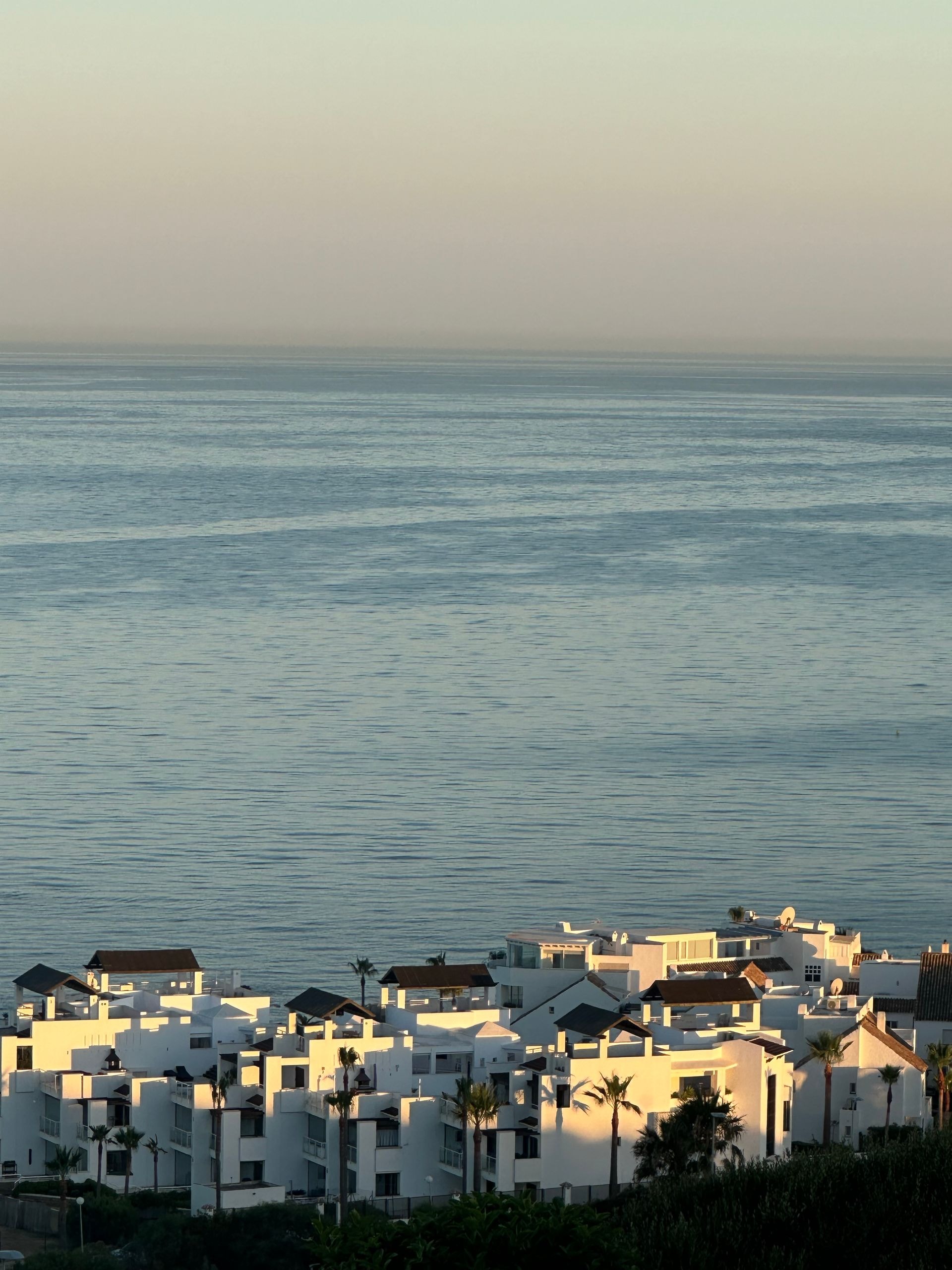Hillside town with white villas overlooking an expansive calm blue sea at dawn