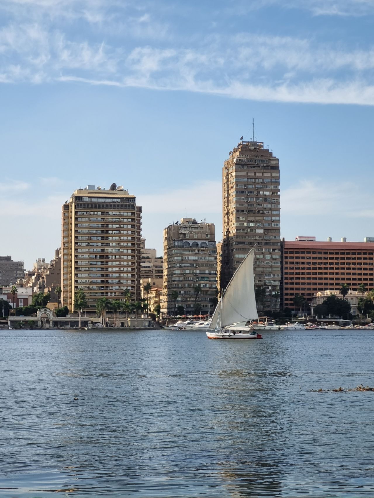 City skyline along the river with sailing boat and waterfront high-rise buildings