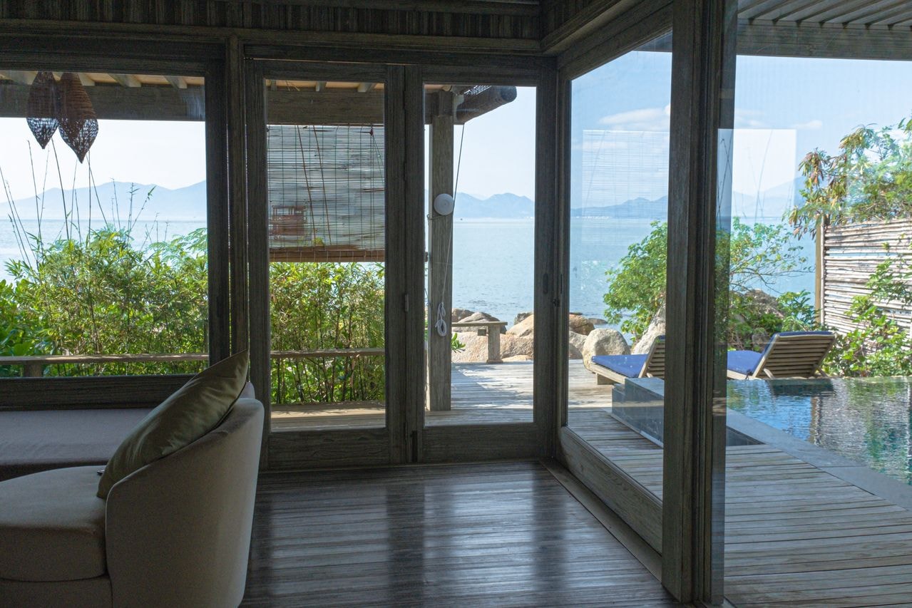 Luxury bedroom suite with floor-to-ceiling glass doors opening onto an infinity pool and ocean view