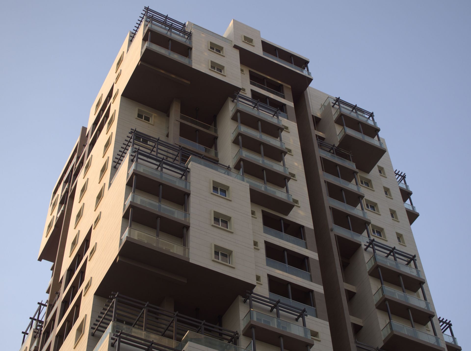 Upward perspective of a modern multi-tiered residential building under clear skies